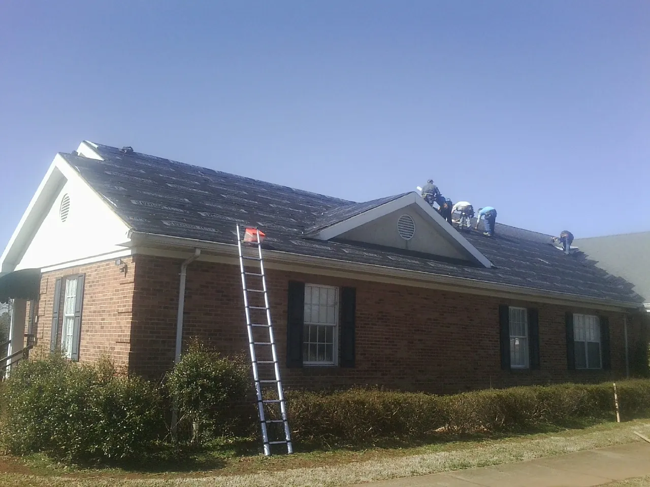 Crew tearing shingles off a brick ranch roof with a ladder set — Metal Roof Repair work by our crew in Evanston