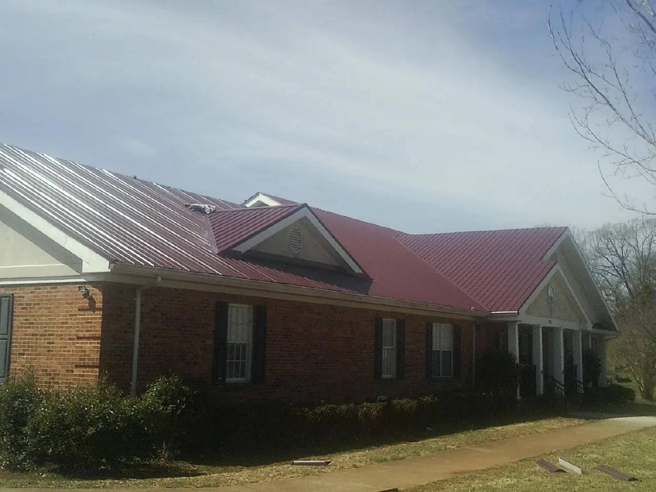Red metal roof with gabled entries on a long brick building, from a Hail Damage Roof Repair job in Evanston