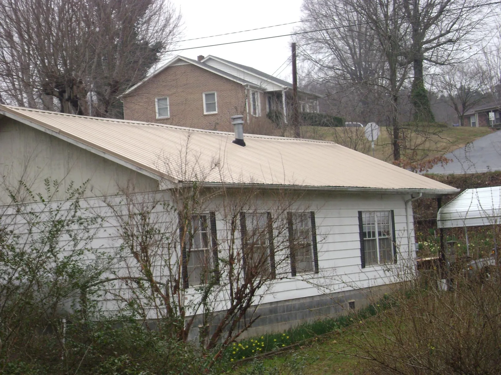 Tan metal roof on a white sided house set into a hillside — Commercial Roofing by Roofing Brothers in Evanston